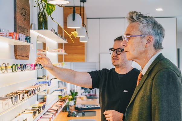 A young optometrist helping a man select from a range of colourful frames