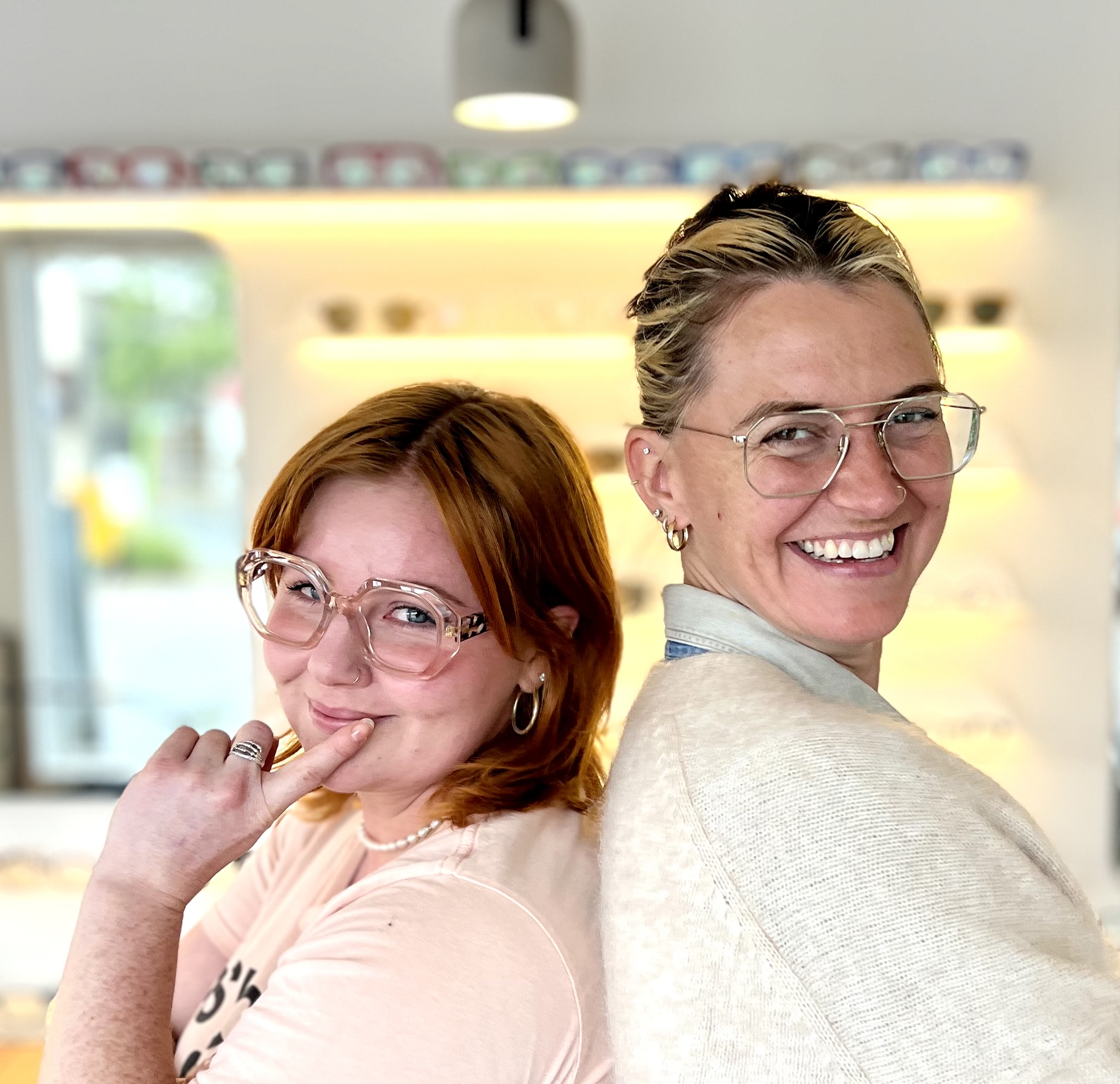 Two stylish young women standing back to back, extremely happy with their eyewear choices