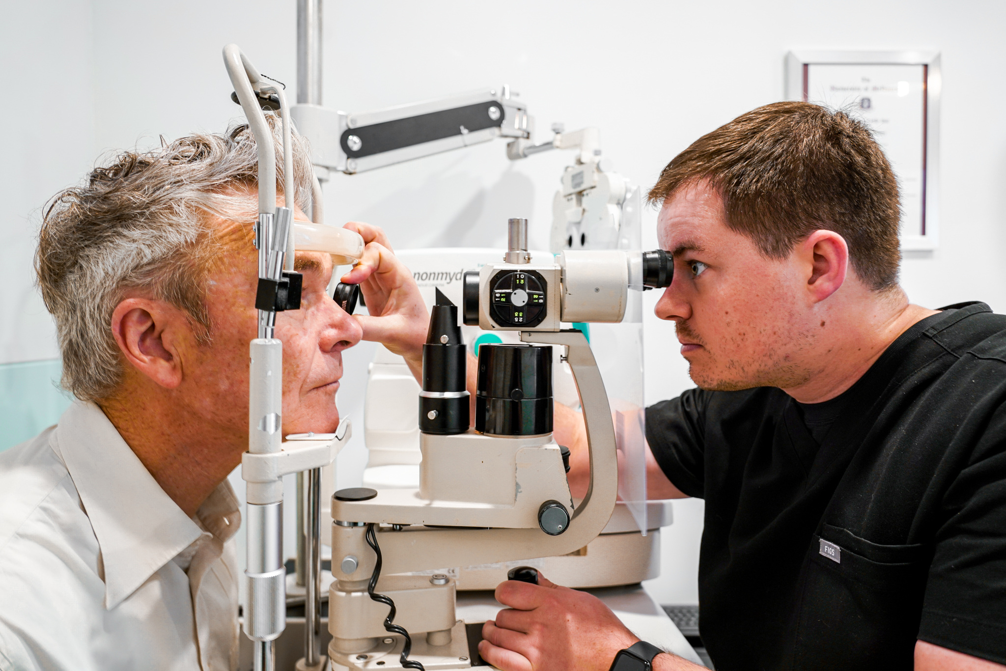 A close up of a male optometrist, examining an elderly patient's eye through a slit lamp